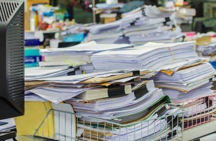 Pile of documents on desk stack up high waiting to be managed